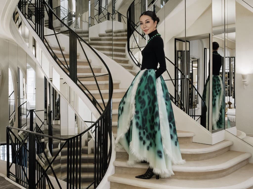 Portrait in a black top and dramatic emerald skirt on a mirrored staircase in a couture maison